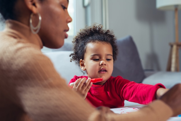 Happy African American mother assisting her daughter in coloring 