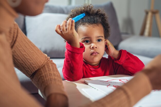 Happy African American mother assisting her daughter in coloring 