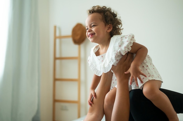 Happy African American mother playing with his girl in bedroom at home