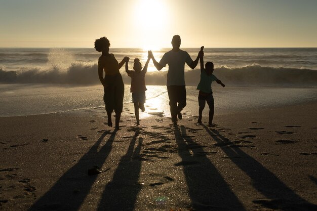 Happy african american parents enjoying sunset with children at beach against sky