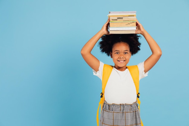 Happy African American schoolgirl holding books above head on blue background back to school concept
