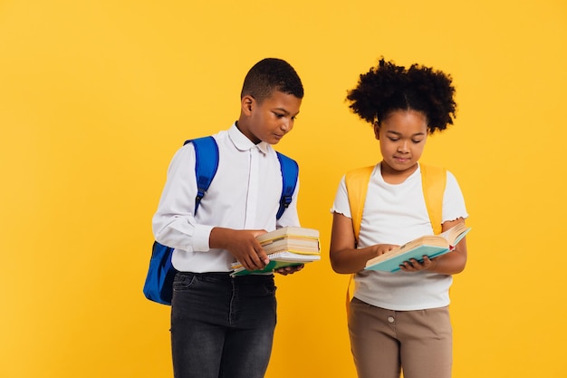 Happy african american schoolgirl and mixed race schoolboy holding books on yellow background copy space