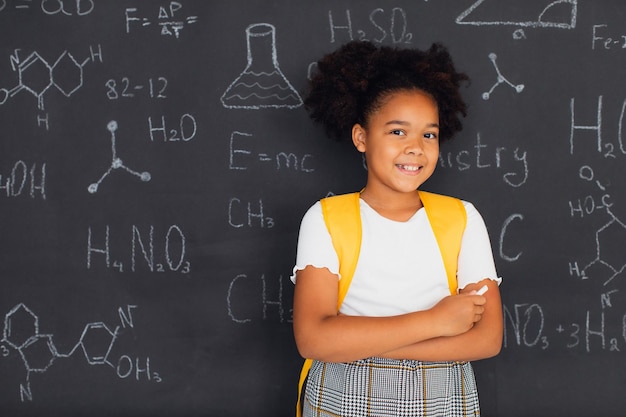Happy African American schoolgirl solving problems near the blackboard at school back to school concept