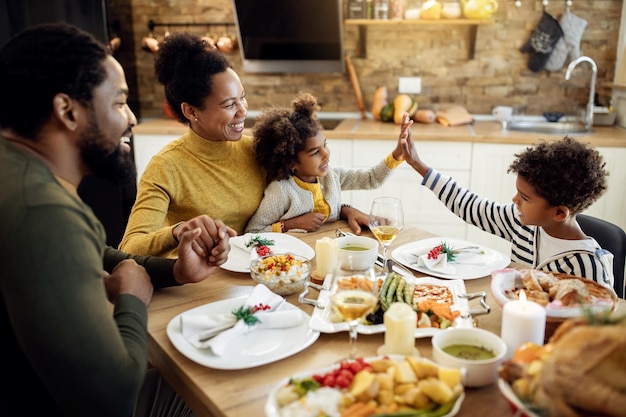 happy african american siblings giving highfive during thanksgiving lunch in dining room