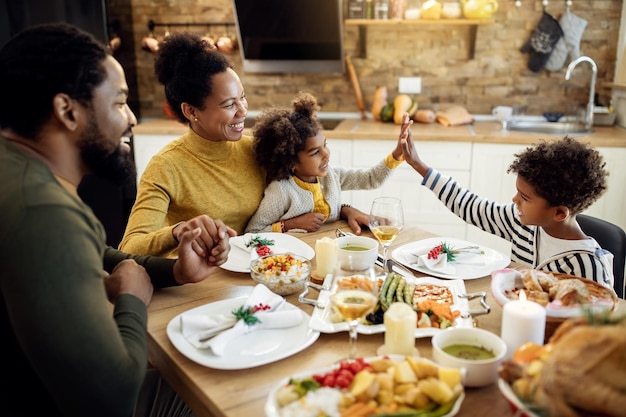 Happy African American siblings giving highfive during Thanksgiving lunch in dining room