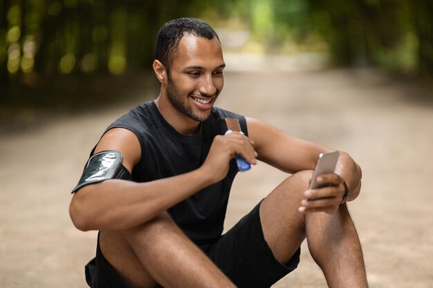 Happy african american sportsman having snack using smartphone