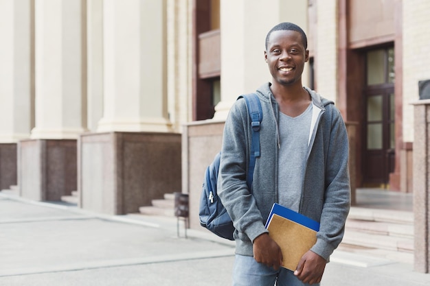 Happy african-american student with books outdoors, looking away, dreaming or thinking during break, having rest in campus. Education concept, copy space