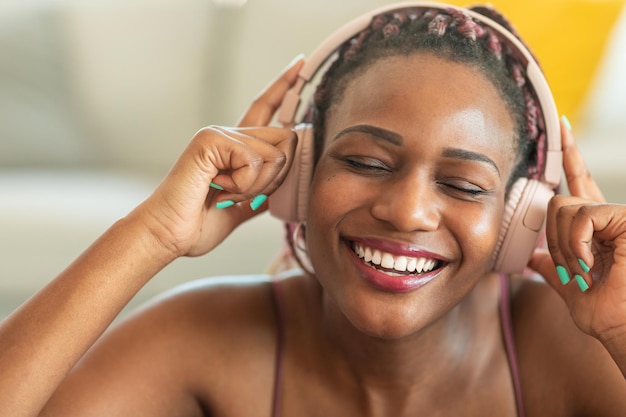 Happy african american woman enjoying music with closed eyes\
touching headphones while resting during home workout