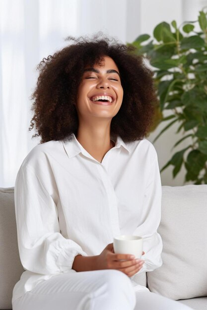 happy african american woman enjoying quiet time at home laughing drinking morning coffee sitting on