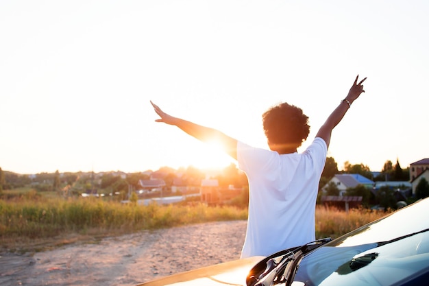 차 근처에 있는 행복한 아프리카계 미국인 여성이 일몰, 생활 방식을 봅니다.