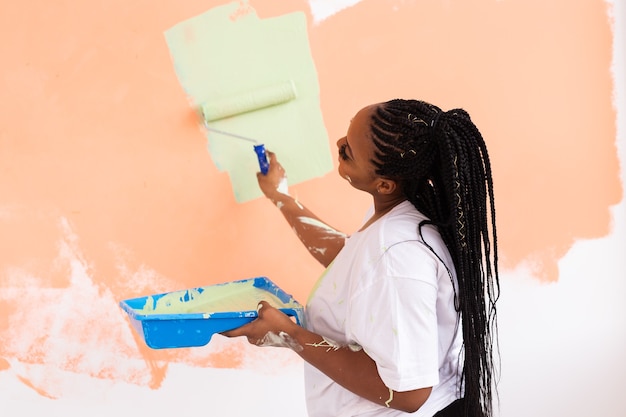 Happy African American woman painting wall in her new apartment. Renovation, redecoration and repair