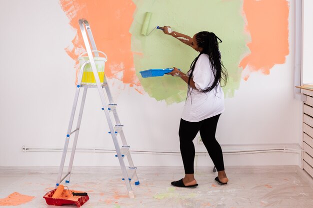 Happy African American woman painting wall in her new apartment. Renovation, redecoration and repair