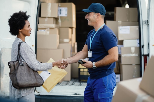 Happy African American woman shaking hands with a courier while getting her package delivered Focus is on man