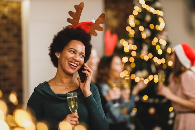 Felice donna afroamericana che parla sullo smartphone alla festa di capodanno in un'atmosfera festosa.