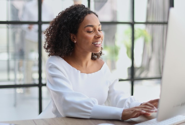 행복한 아프리카계 미국인 여성이 노트북을 사용하여 사무실에서 공부하고 일합니다.