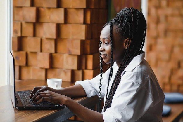 Happy african american woman worker using laptop work study at computer in loft office or cafe, smiling mixed race female student freelancer using pc app dating communicating online watching webinar