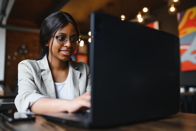 Счастливая африканская американка-работница, использующая ноутбук, учится за компьютером в лофт-офисе или кафе, улыбается, студентка смешанной расы, фрилансер, использующая приложение для ПК, знакомится, общается онлайн, смотрит вебинар