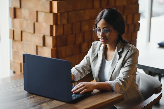 로프트 사무실이나 카페에서 노트북 작업을 하는 행복한 아프리카계 미국인 여성 근로자는 온라인 시청 웹 세미나를 시청하는 PC 앱 데이트를 사용하여 웃고 있는 혼혈 여학생 프리랜서