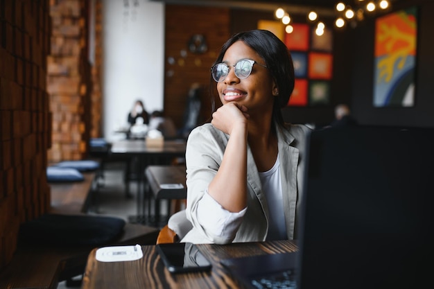 Happy african american woman worker using laptop work study at computer in loft office or cafe smiling mixed race female student freelancer using pc app dating communicating online watching webinar