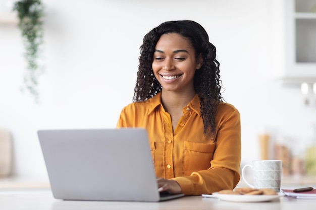 Счастливая африканская американка, работающая дома с помощью ноутбука