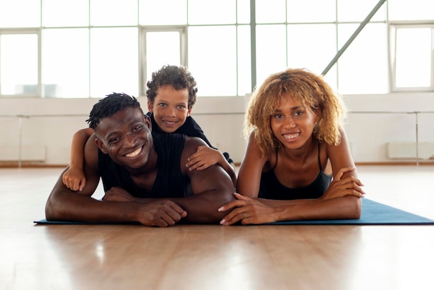 Photo happy african american young family lies and rests on yoga mat in the gym mom dad and son