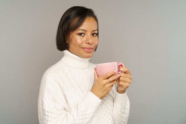 お茶を飲むマグカップからおいしいコーヒーを楽しんで広く笑っている幸せなアフリカ系アメリカ人の若い女性