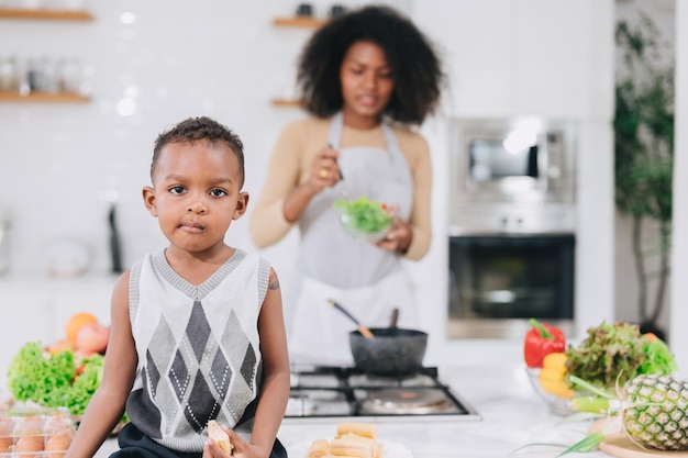 Happy african black young mother with her boy lovely cute cooking together at home holiday activity