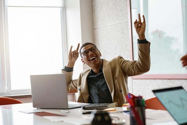 Foto felice uomo d'affari africano con gli occhiali che lavora al computer portatile mentre è seduto in un moderno coworking