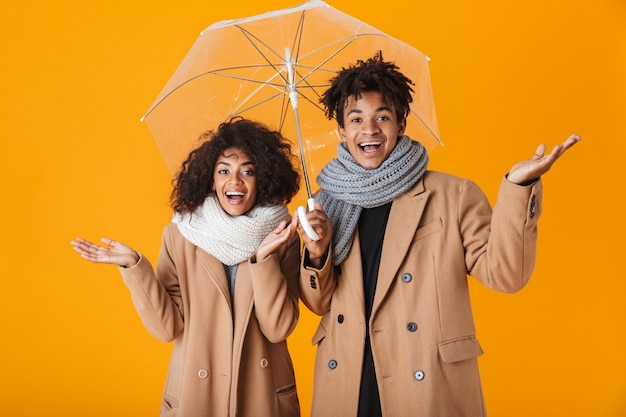 Happy african couple wearing winter clothes standing under an umbrella isolated