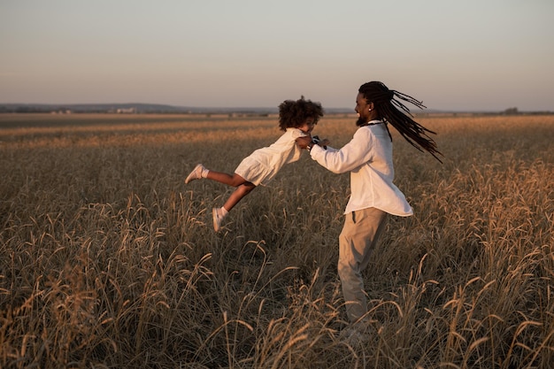 Foto un padre africano felice fa girare sua figlia tra le braccia in un campo