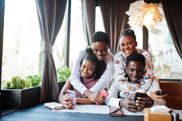 Happy african friends sitting and chatting in cafe Group of black peoples meeting in restaurant hugs and look at their mobile phone