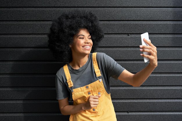 Happy african girl blogger holding smartphone shooting vlog or video calling