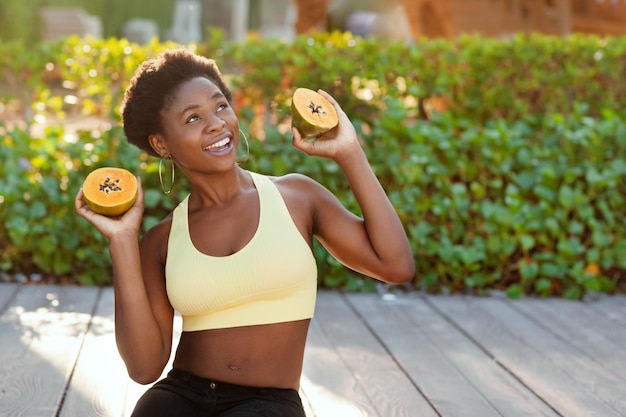 Счастливая африканская девушка сидит снаружи и держит свежую папайю в руках