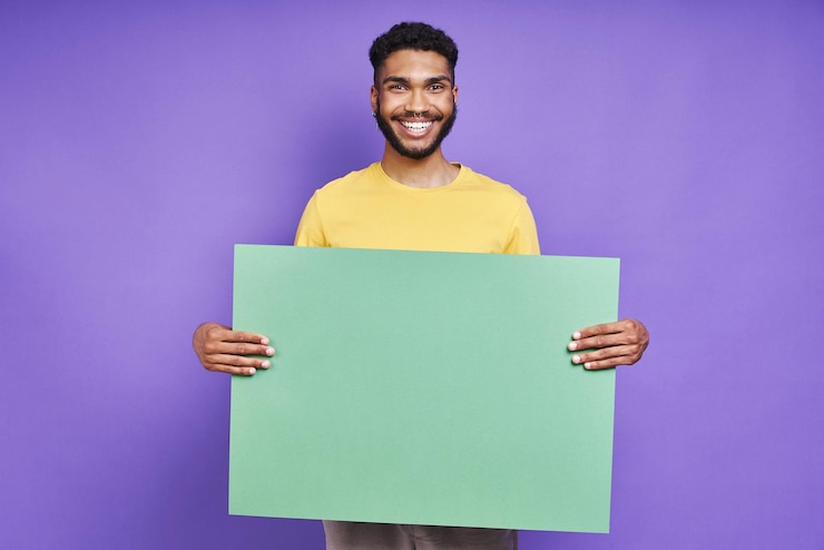 Photo happy african man holding green banner while standing against purple background