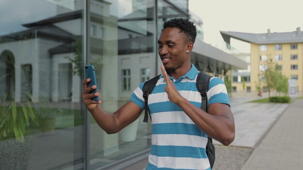 Happy african man video talking with friend online on the\
mobile phone in the urban street portrait of positive man talking\
in city