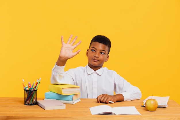 Happy african schoolboy sitting at desk and stretching arm up during class Back to school concept