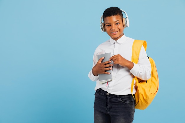 Happy african schoolboy wearing headphones and backpack holding books and notebooks