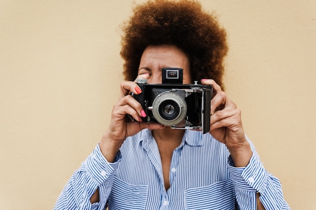 Happy african senior woman using vintage camera outdoors in the city - Focus on face