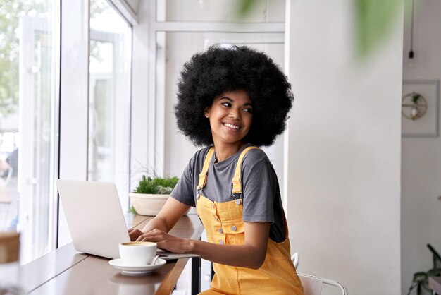 happy african teen girl student using laptop sit at table in cafe with coffee