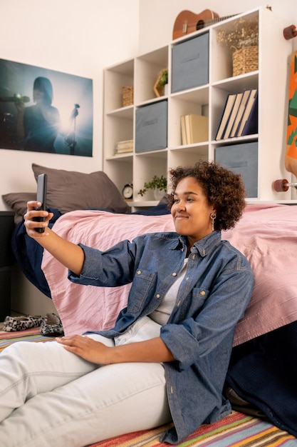 Happy african teenager with smartphone communicating in videochat