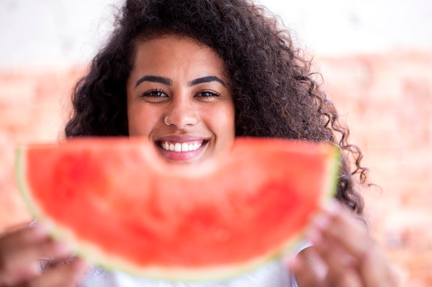 Happy african woman in the kitchen and holding slice of a watermelon  