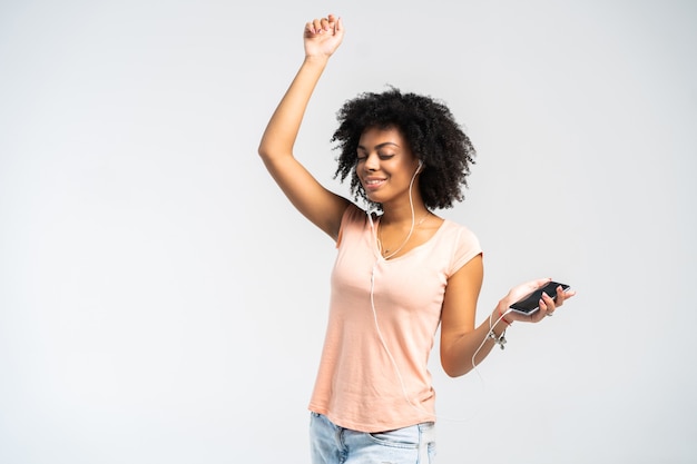 Happy african woman with afro and casual clothing dancing to the music she is listening to from her phone.