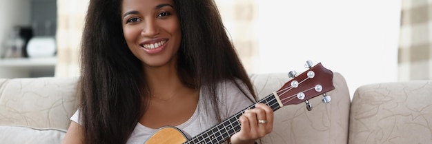 집에서 거실에서 우쿨렐레를 연주하는 행복한 아프리카계 미국인 여성