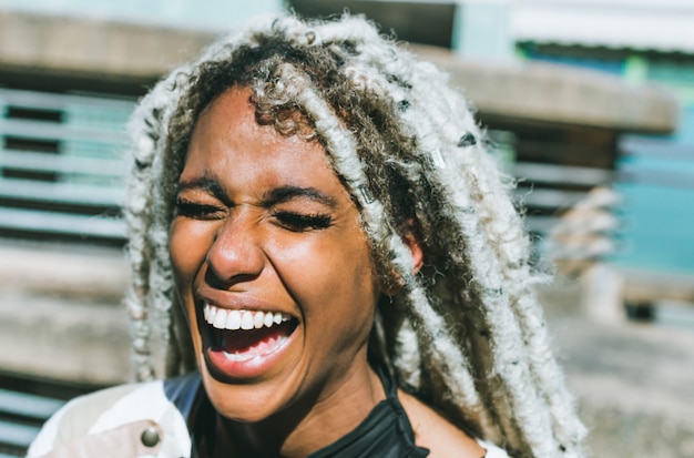 Happy afro girl with blond dreadlocks laughing outdoors