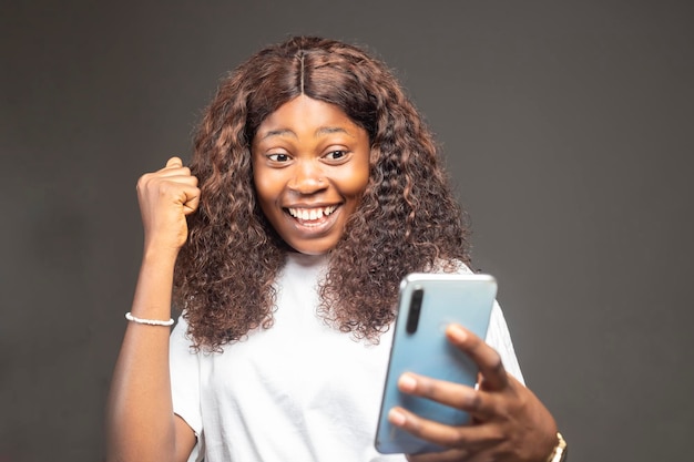 회색 배경 스튜디오 샷 좋은 뉴스 개념 위에 스마트폰을 들고 있는 행복한 아프리카 밀레니엄 여성