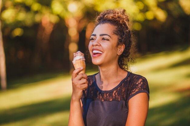 Happy afro woman eating ice cream in the park