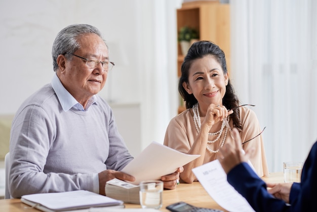 Happy aged couple meeting with real estate manager filling document and making payment for new house