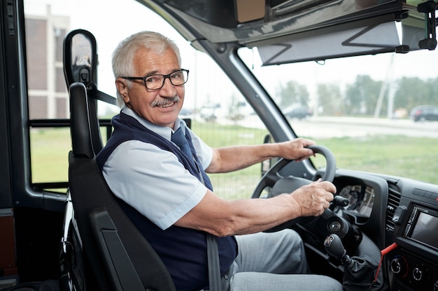 Счастливый пожилой водитель междугороднего автобуса, держащийся за руль