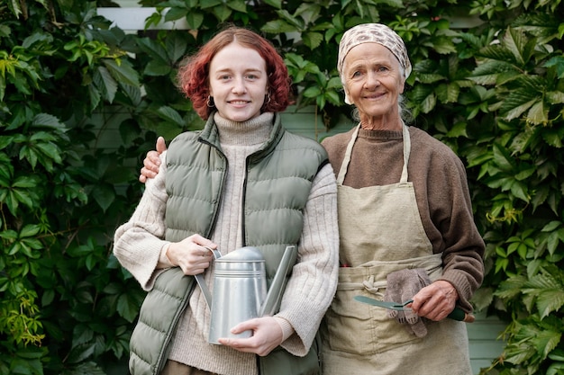 Happy aged woman and her granddaughter with wateringpot looking at you