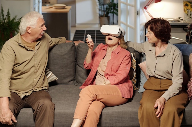 Happy aged woman in vr headset pressing button on remote control